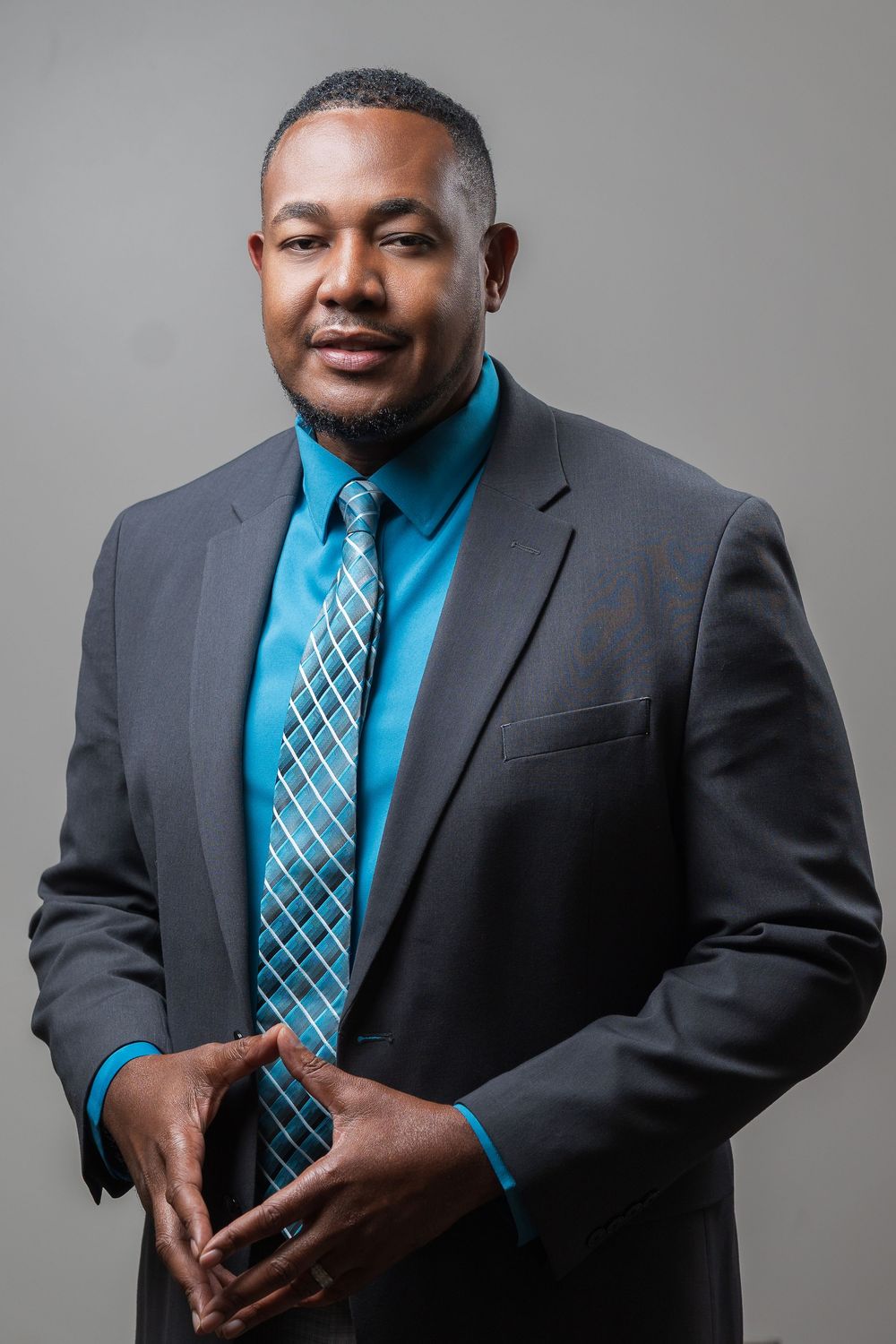 Professional studio portraits of a person in a charcoal suit and bright turquoise dress shirt with patterned tie against gray backdrop.