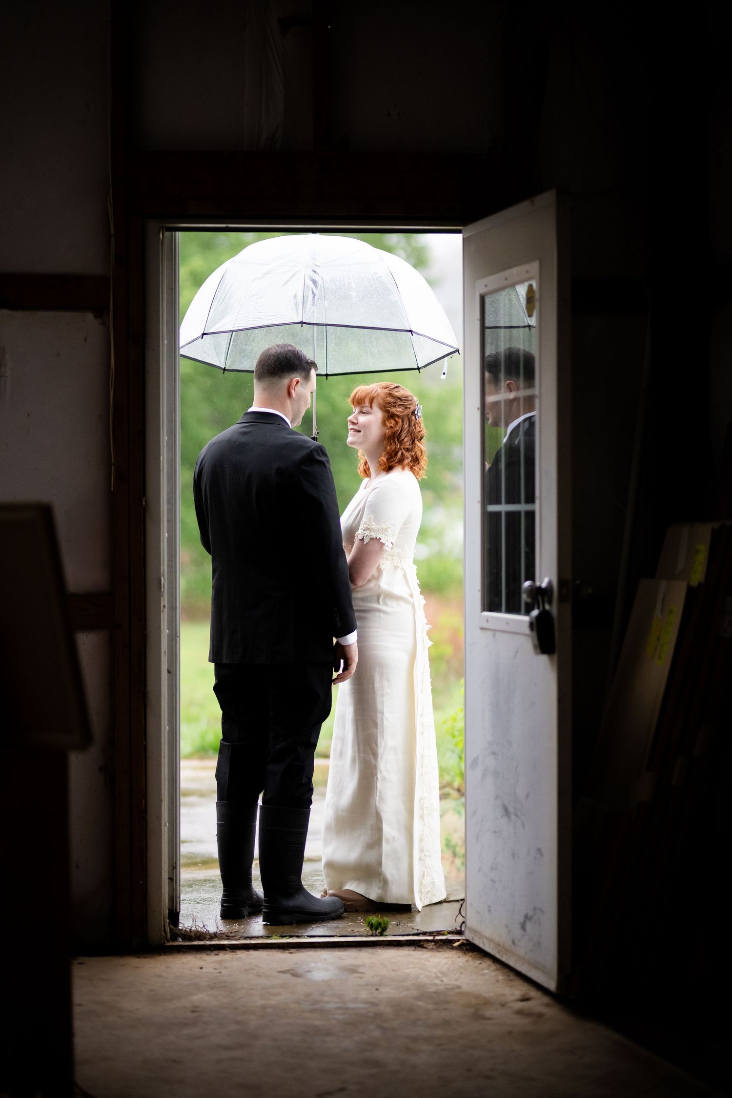Bride and groom under an umbrella in a doorway on a rainy day at their White River riverside wedding in Arkansas