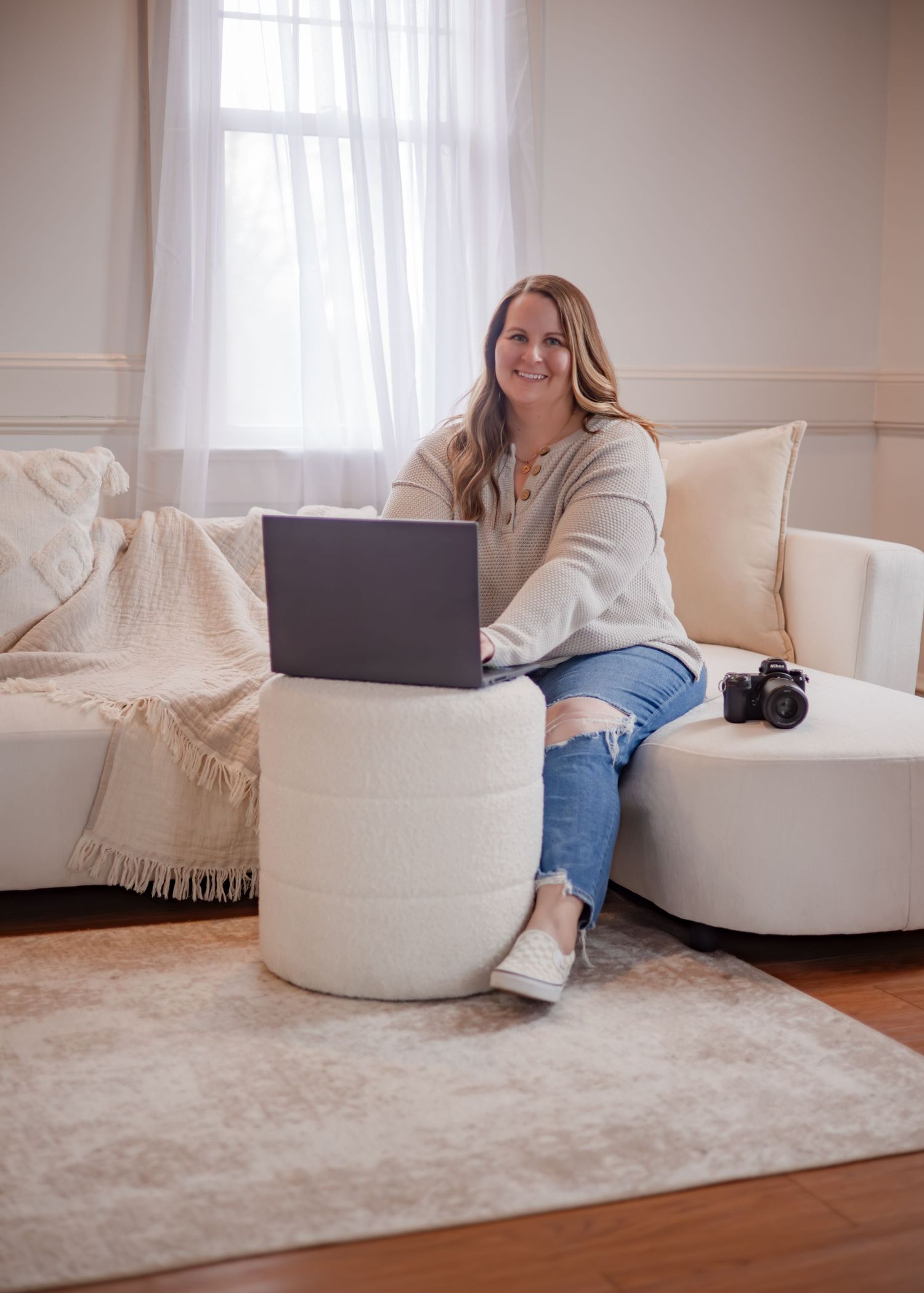 Branding headshot of photographer sitting on couch with her camera next to her while laptop sits open in front of her. Wrightstown NJ