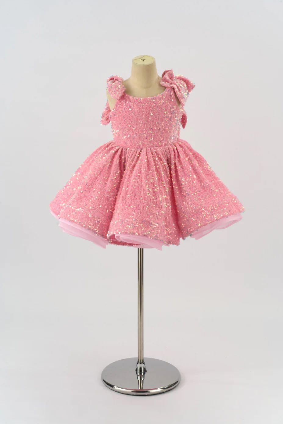 Pink sparkly dress with flutter sleeves displayed on a silver dress form stand against white background.