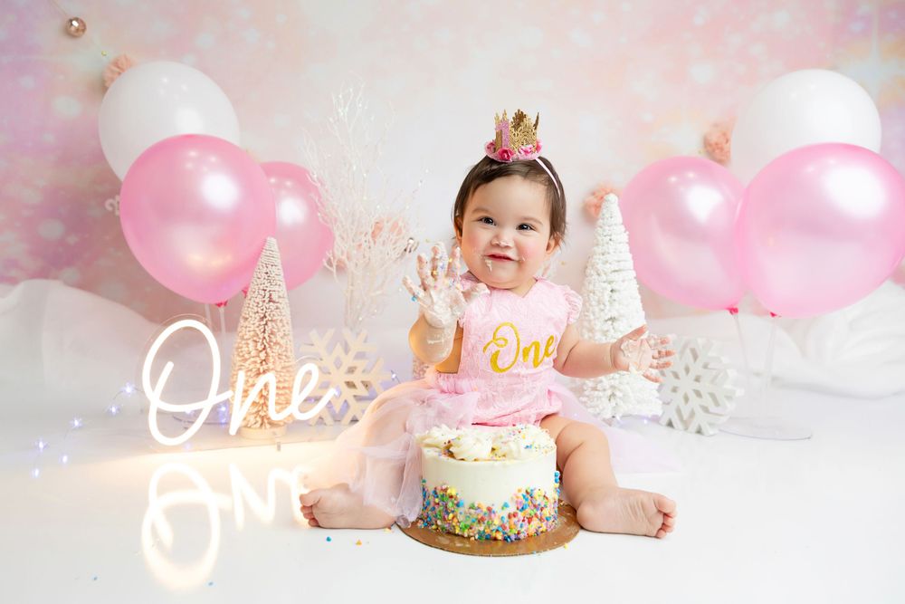 First birthday cake smash setup with pink balloons and gold decorative elements.