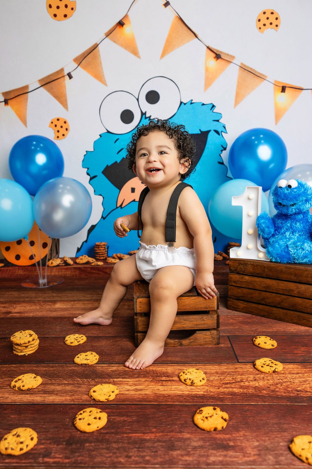 Cookie Monster themed first birthday with orange banners and scattered cookies on wood floor.
