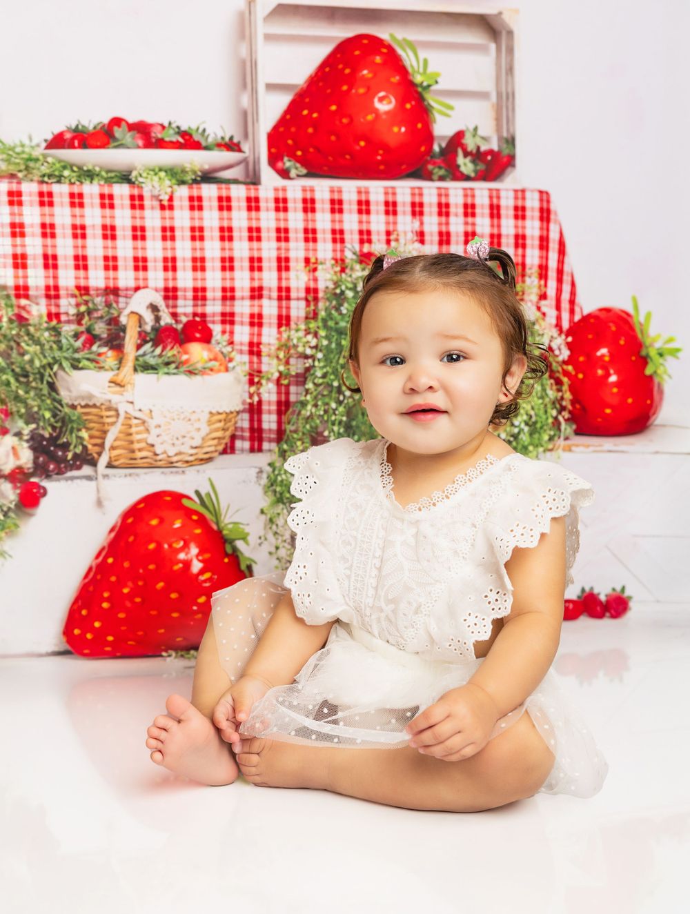 Birthday photo setup featuring large strawberry decorations, gingham tablecloth, and rustic wooden crates.