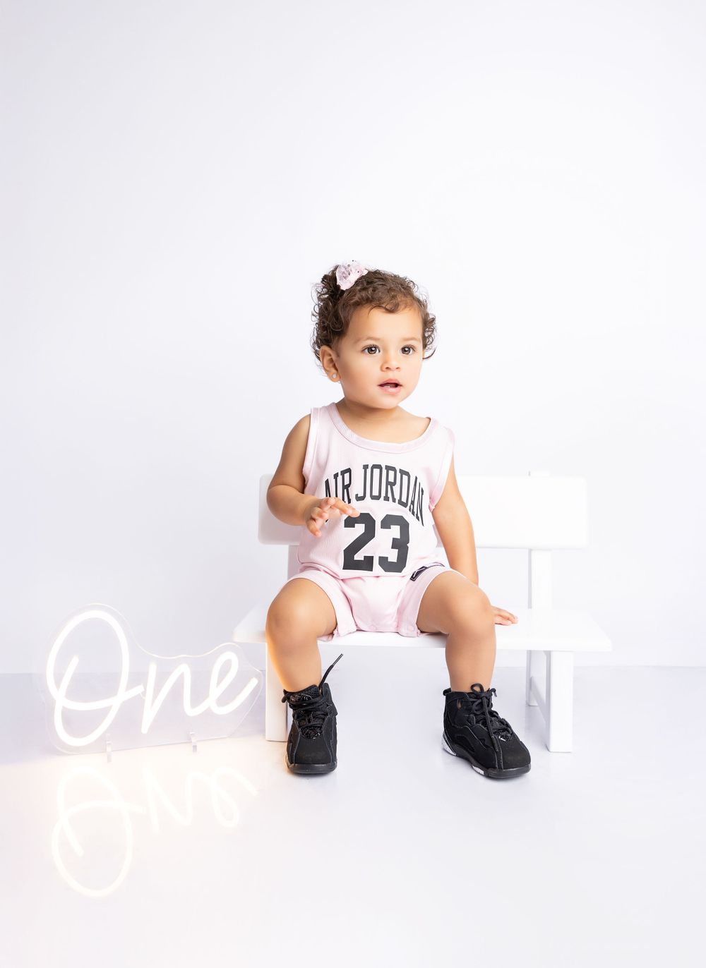 Child wearing Air Jordan 23 jersey sits on white cube against plain background.