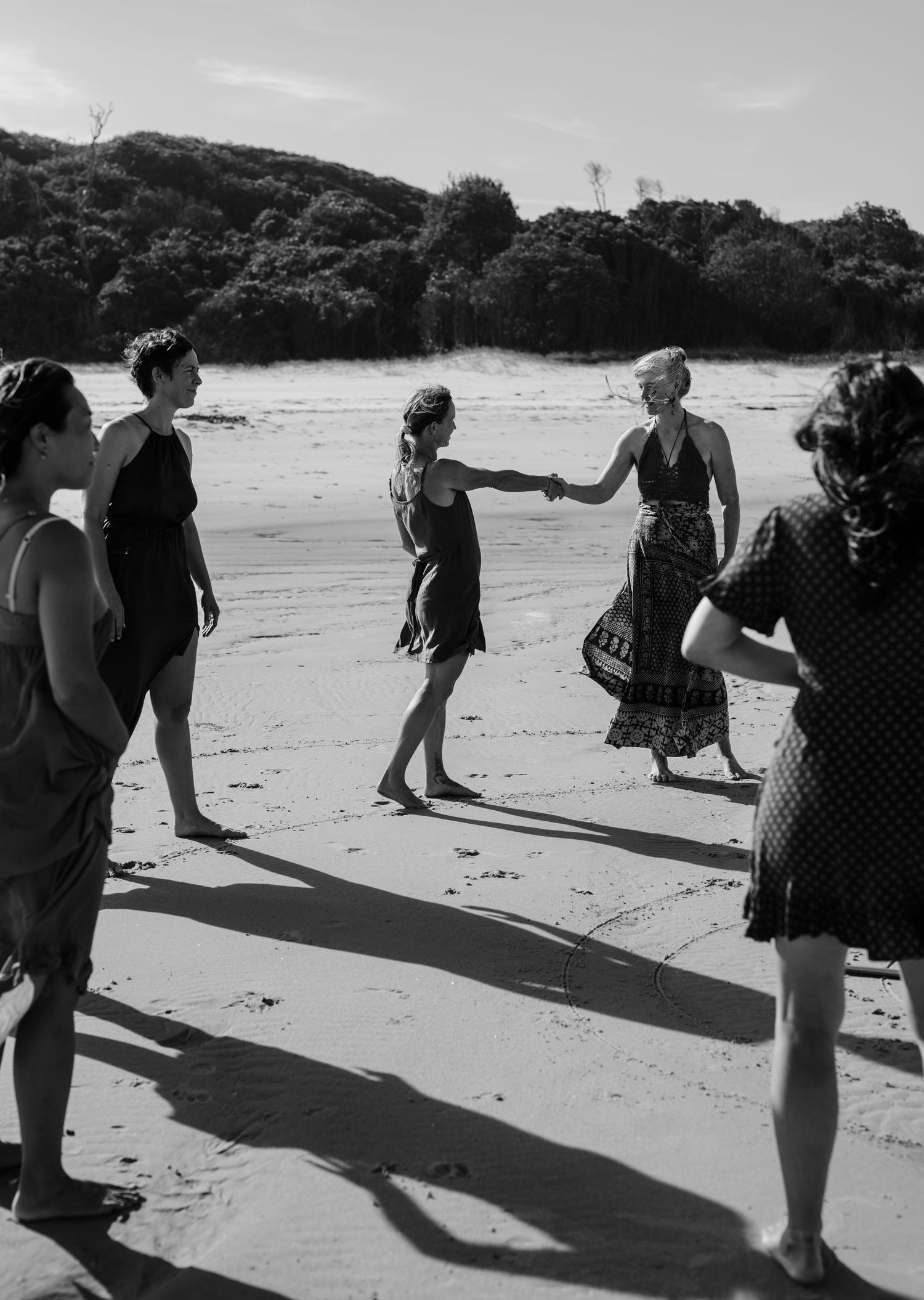 People cast long shadows while walking in a line formation on a sunny beach.