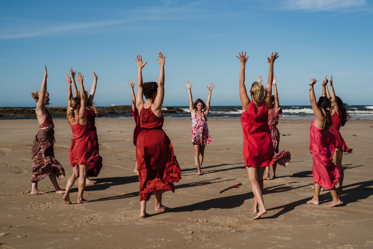 Group performs coordinated dance movements on a beach wearing matching red attire.