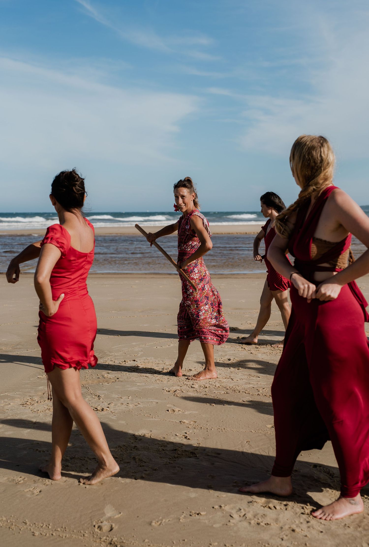 Group in red dresses playfully posing and dancing on a sunny beach.