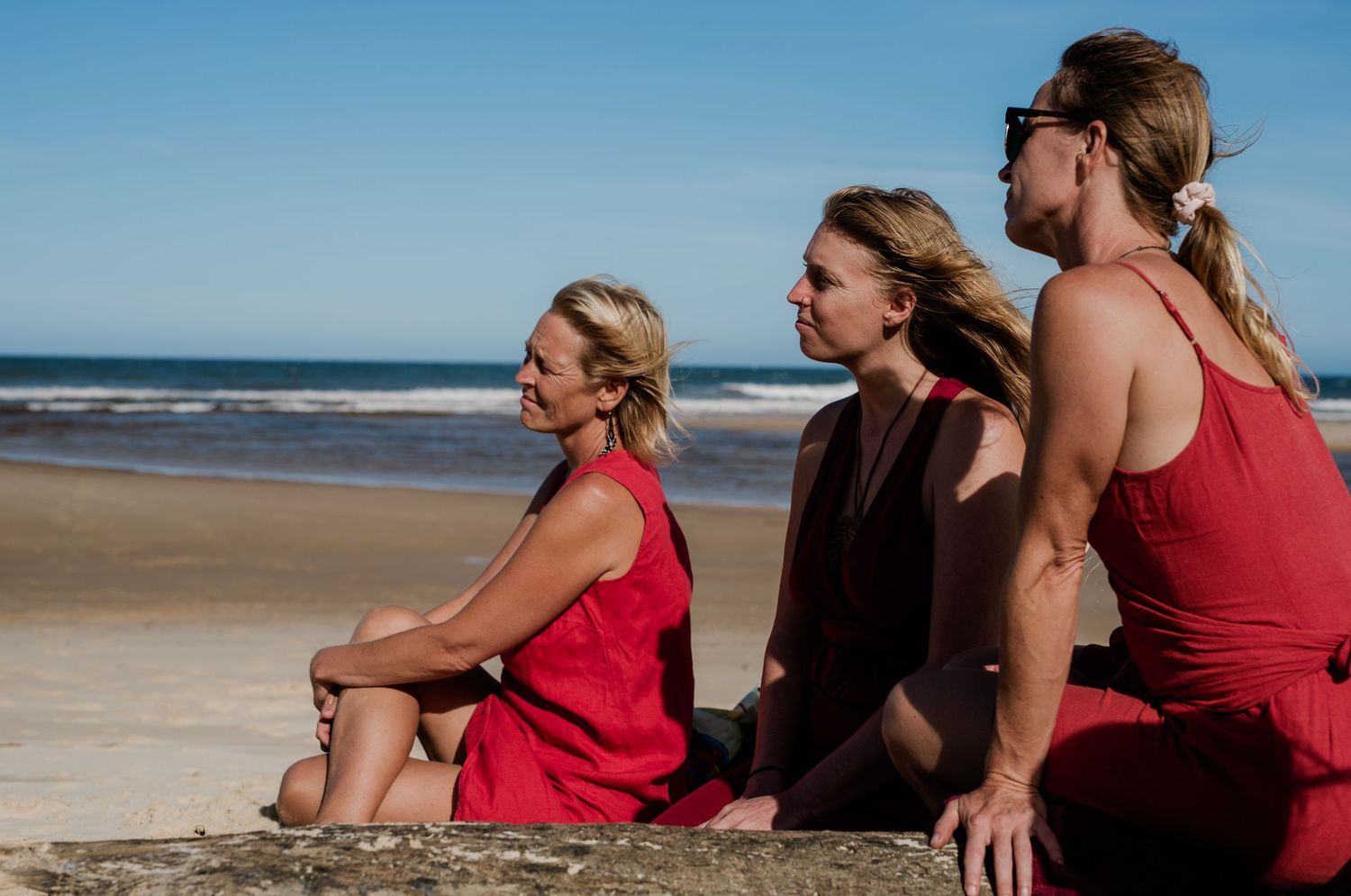 Group of people sitting together on a sandy beach looking out at the ocean.