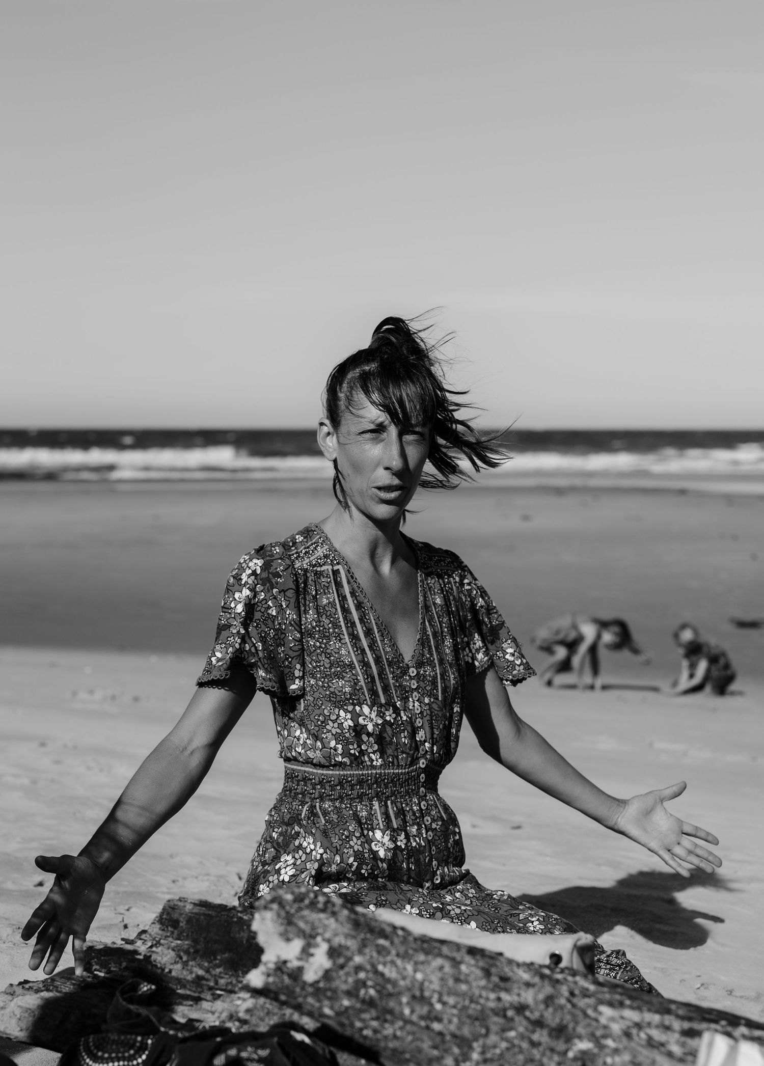 Person in a patterned dress dances expressively on a beach with waves in the background.