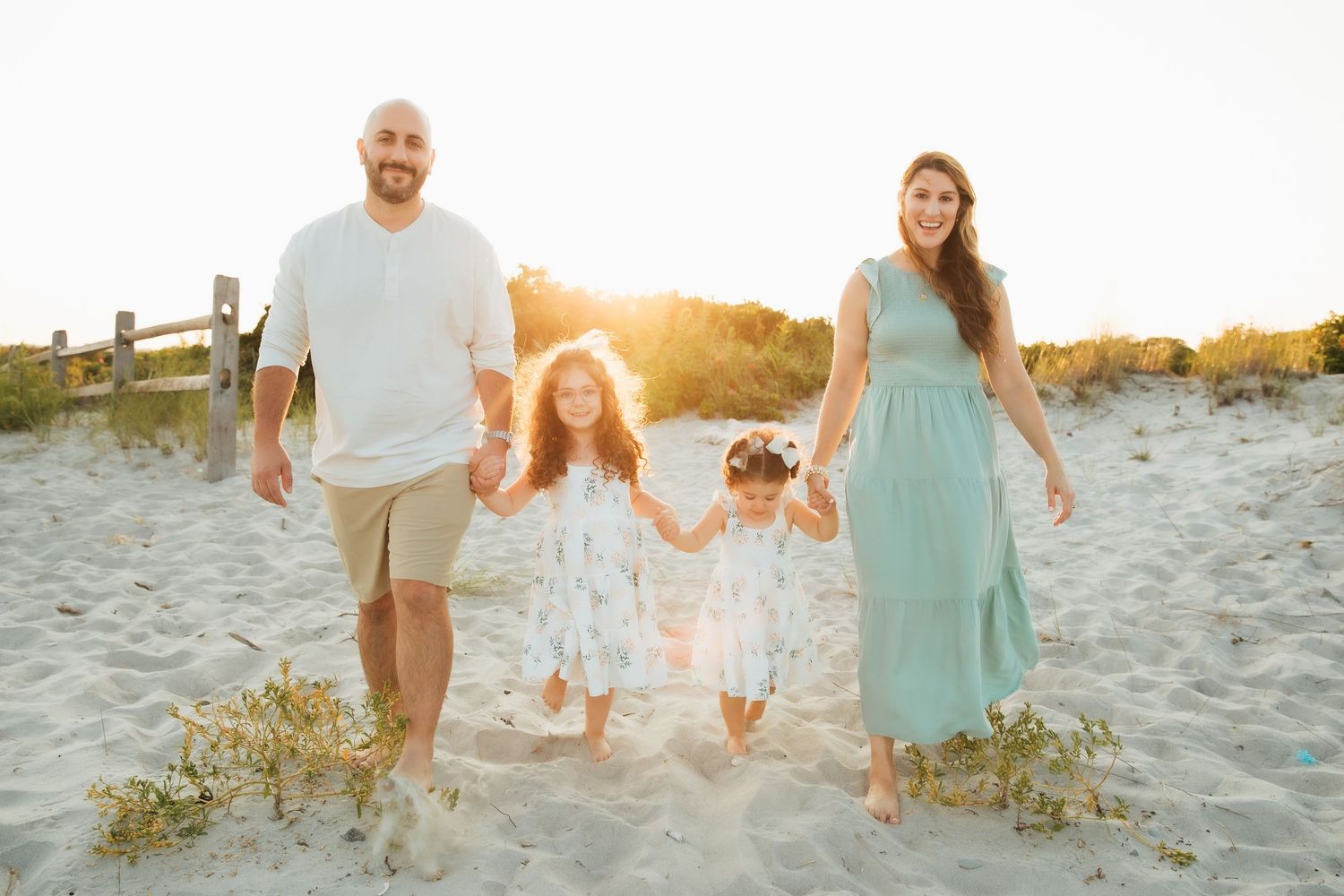 Family walks together on sandy beach at sunset holding hands in casual coastal attire. family photoshoot, Middletown RI Third Beach