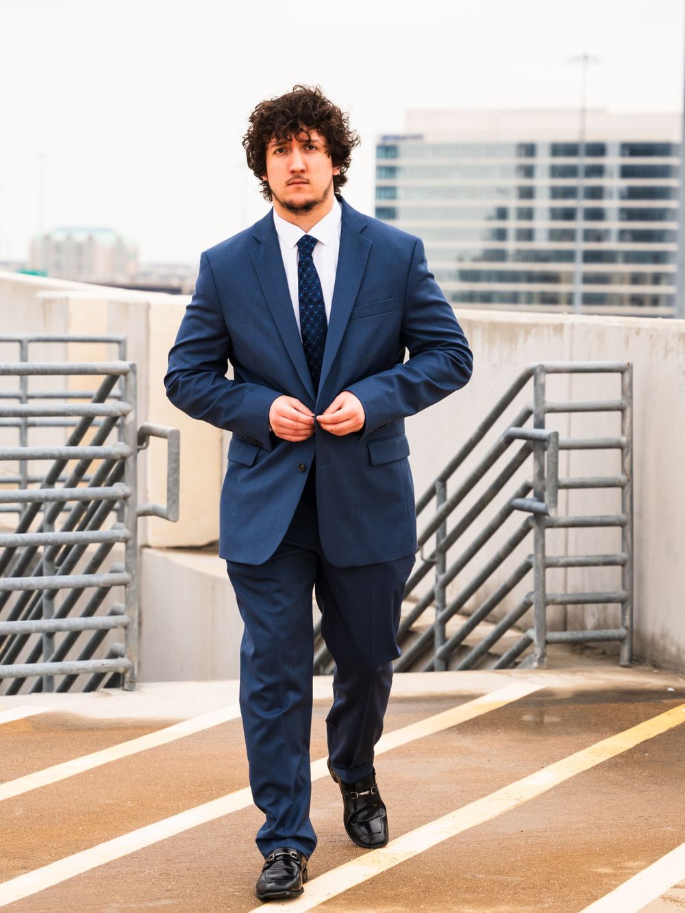 Professional walking across rooftop parking area in navy business suit.