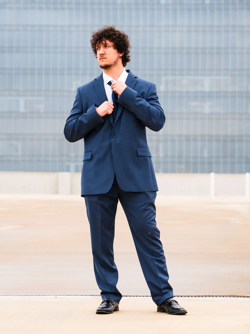 Professional wearing navy blue suit stands confidently against modern urban backdrop.
