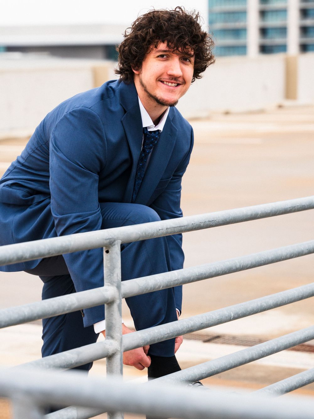 Person in blue suit leans casually against metal railing in urban setting.