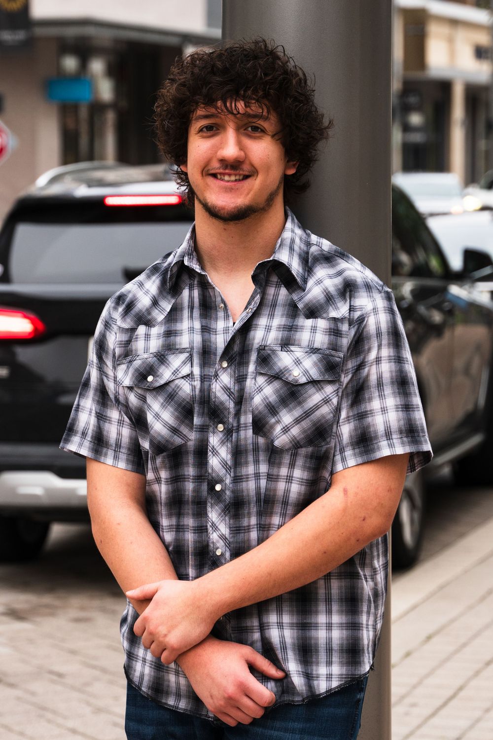 Portrait of someone wearing black and white plaid shirt standing on city street.