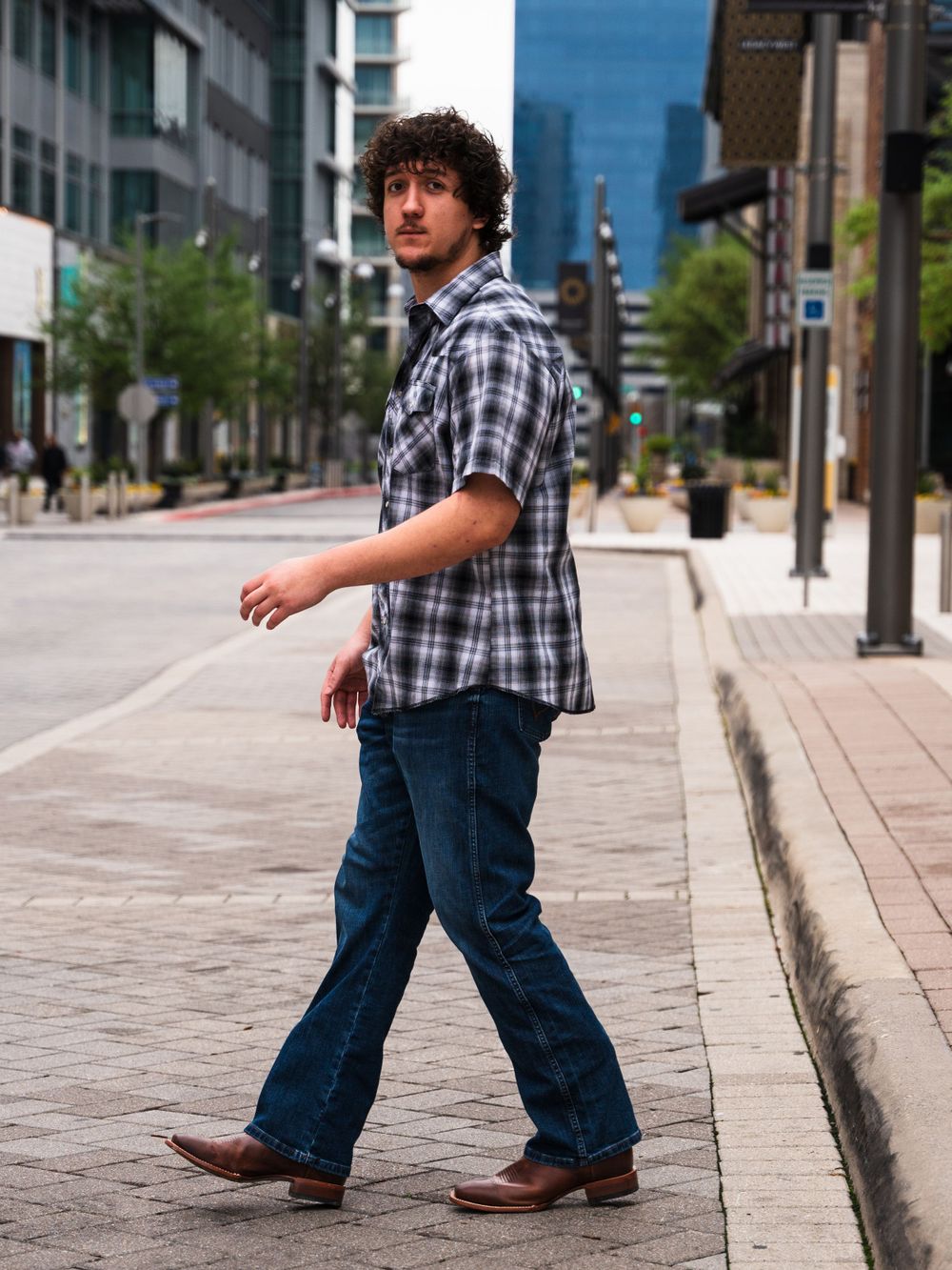 Candid shot of person in plaid shirt walking on downtown sidewalk.
