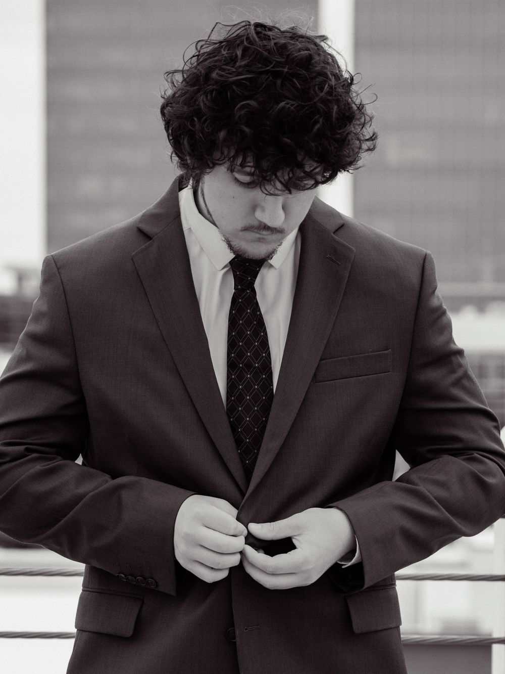 Black and white portrait of person in dark suit adjusting tie.