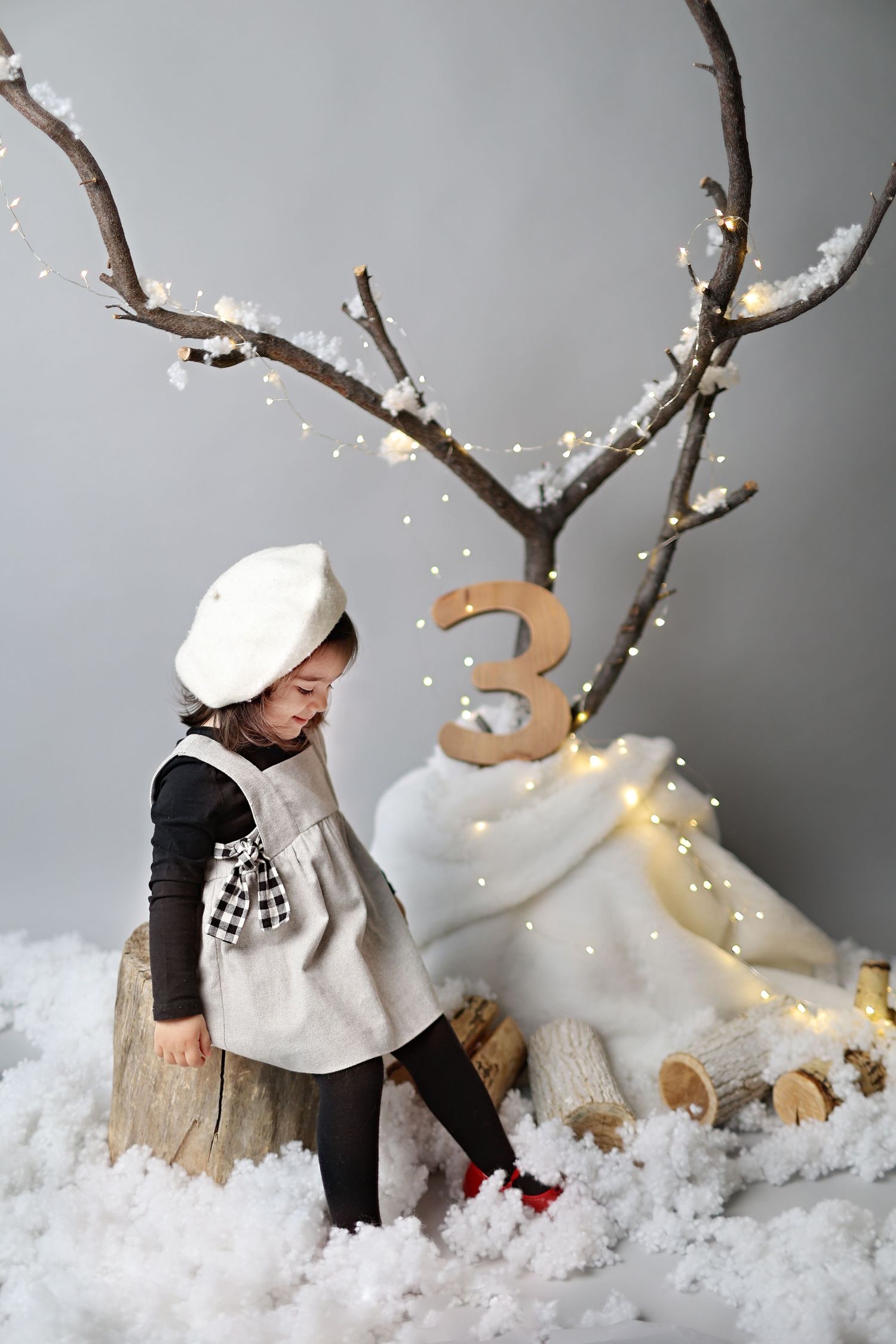 Child in winter attire explores snowy scene with lit branches and number three decoration.