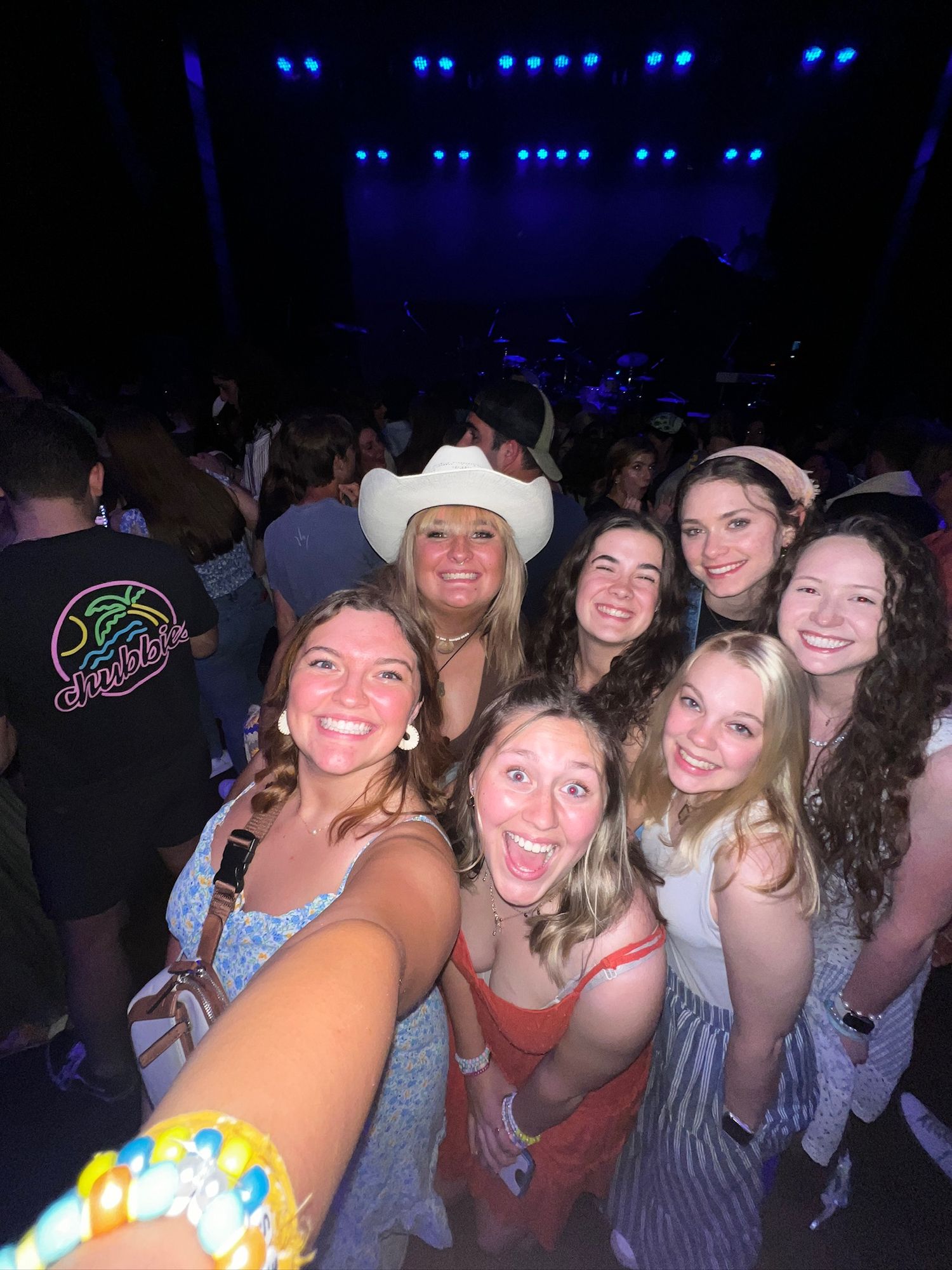 A group of concert-goers enjoy a live show with blue stage lighting visible in the background.