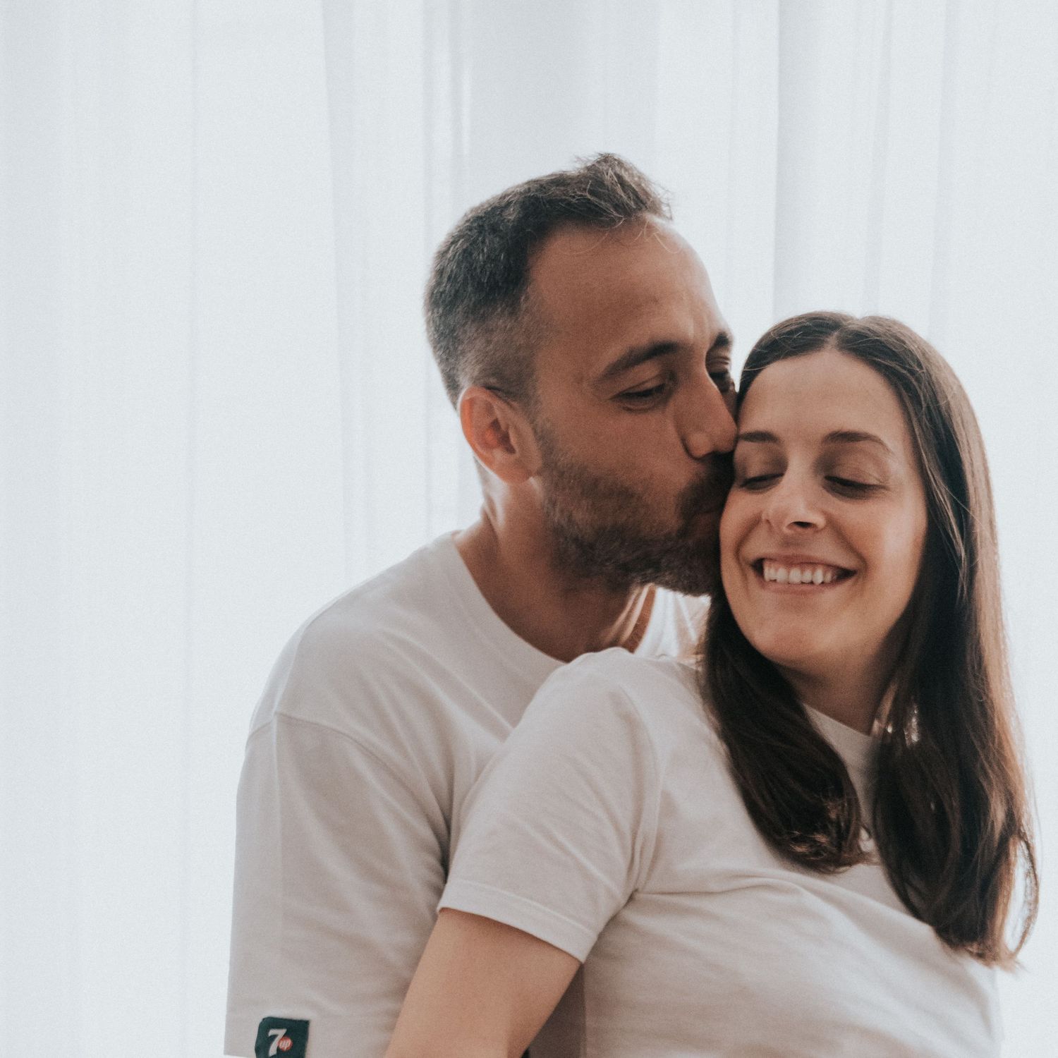 Happy couple sharing intimate romantic moments together in white bedroom setting.