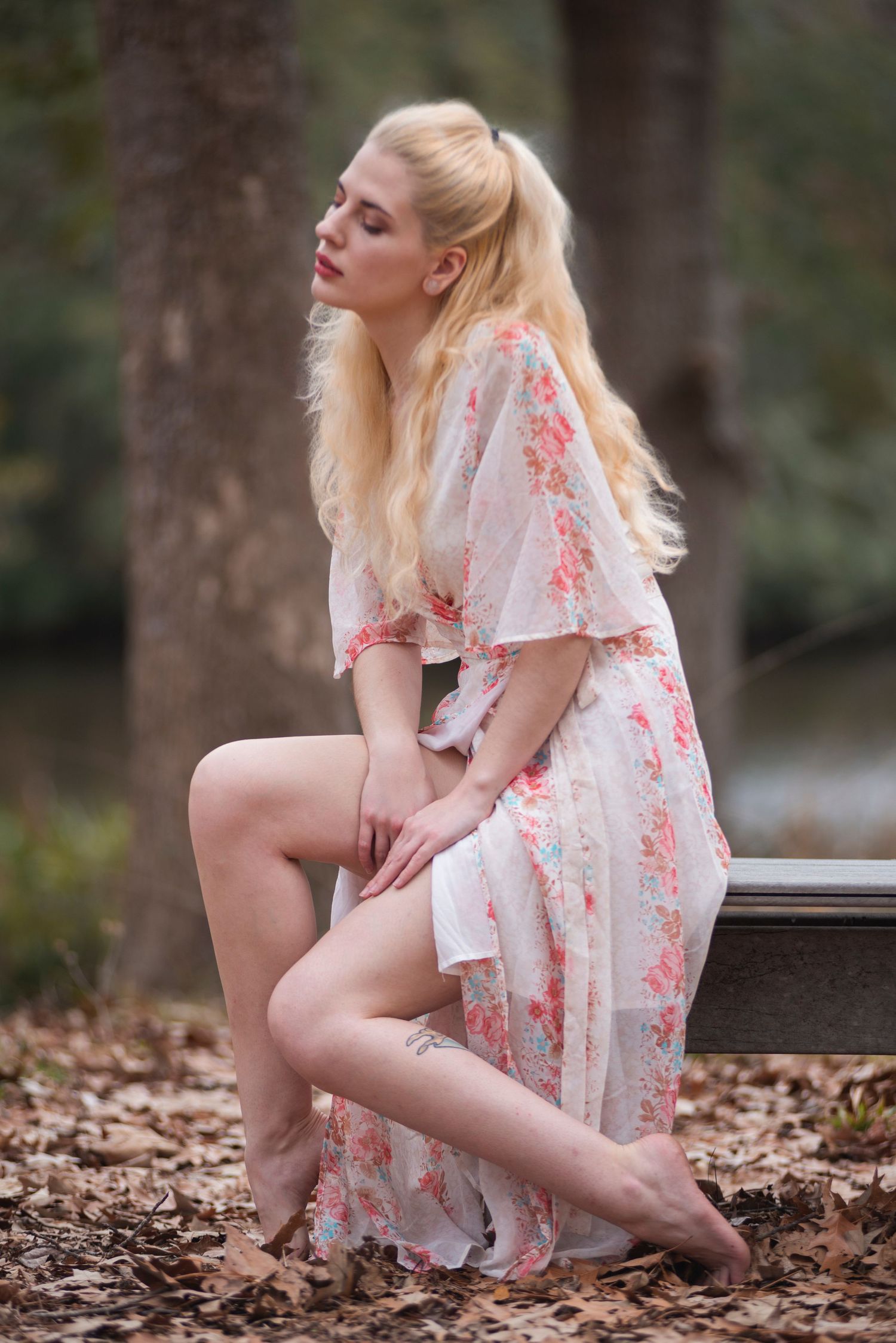 Woman in floral dress poses gracefully in autumn forest setting.