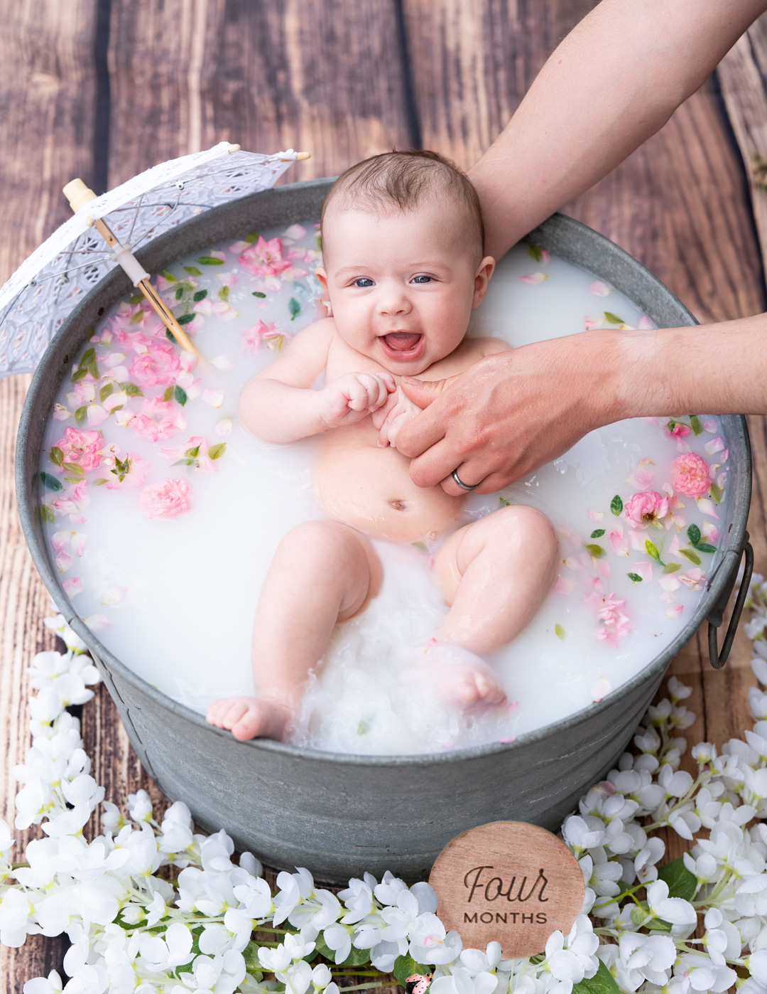 Baby milk bath photography session with floral decorations in a rustic metal tub.