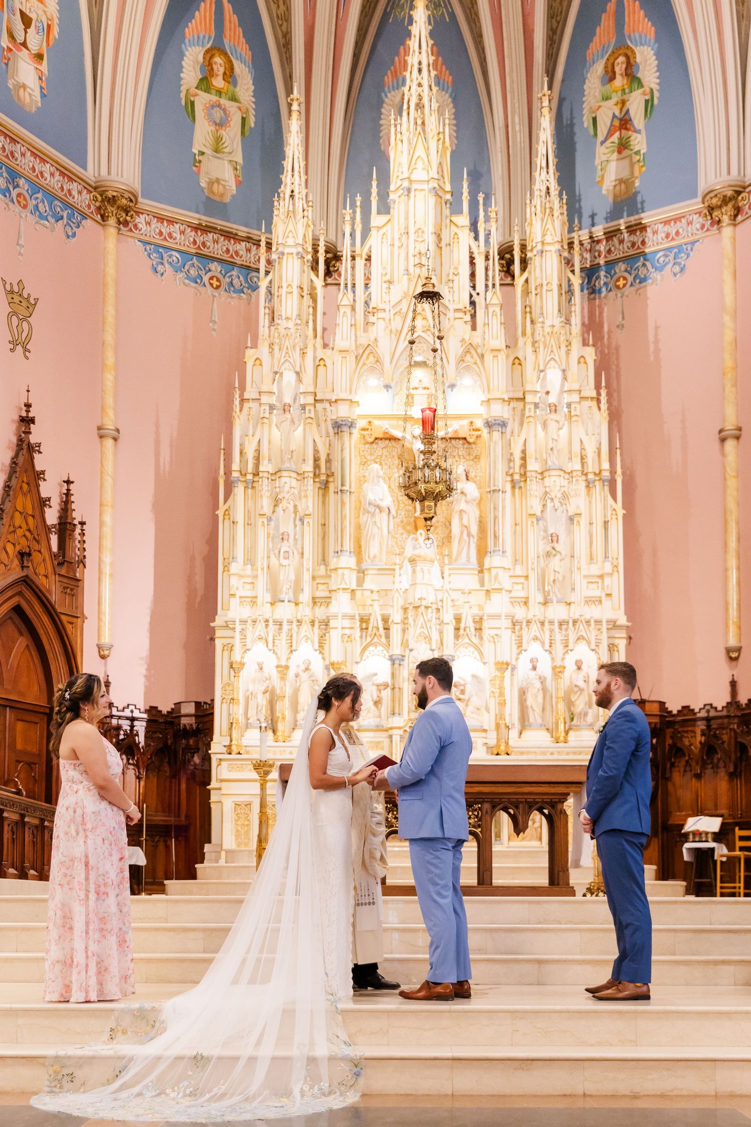 Wedding ceremony in ornate cathedral with elaborate white gothic altar and vaulted ceiling.