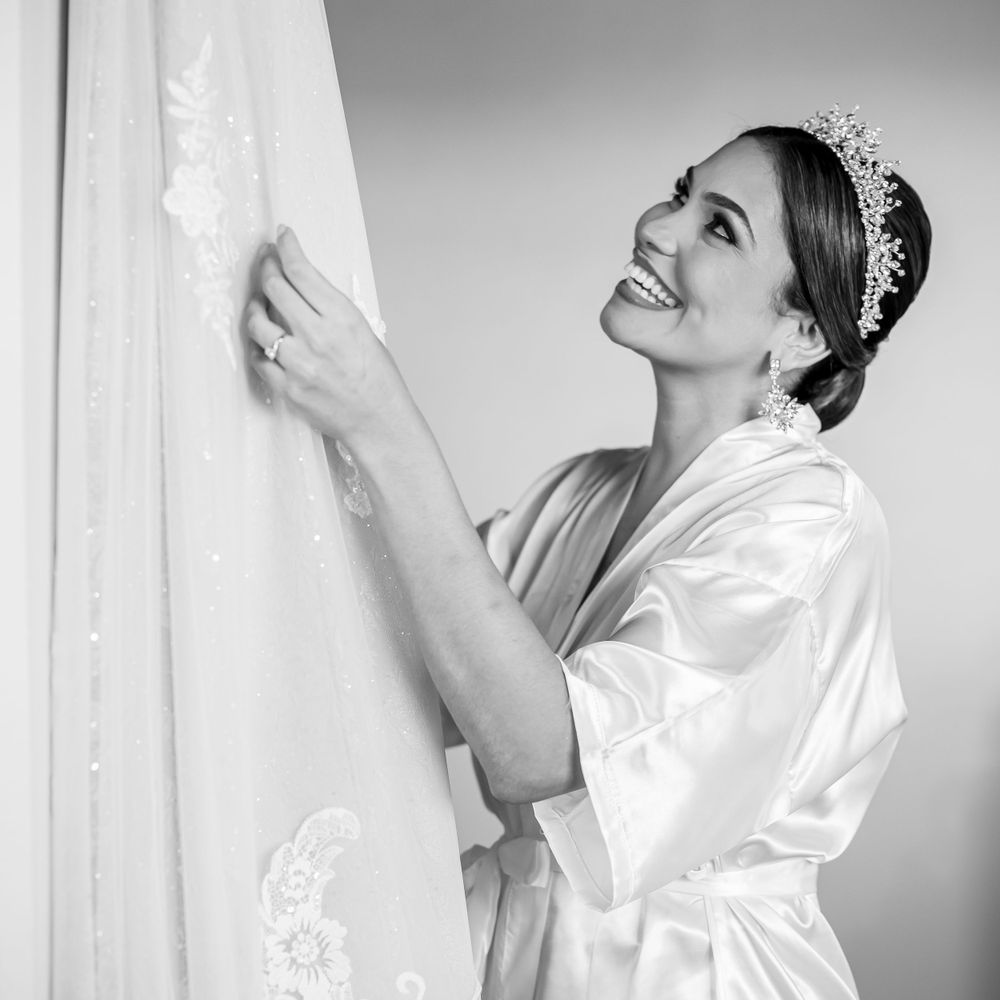 A person in silk robe admiring wedding dress with joy while wearing tiara.