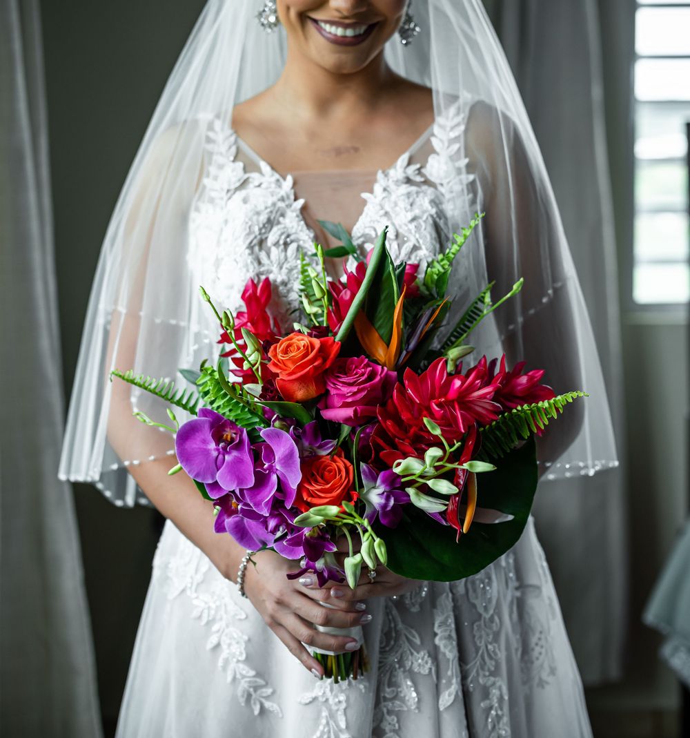 Bride in lace gown holding vibrant bouquet with purple, red and orange flowers.