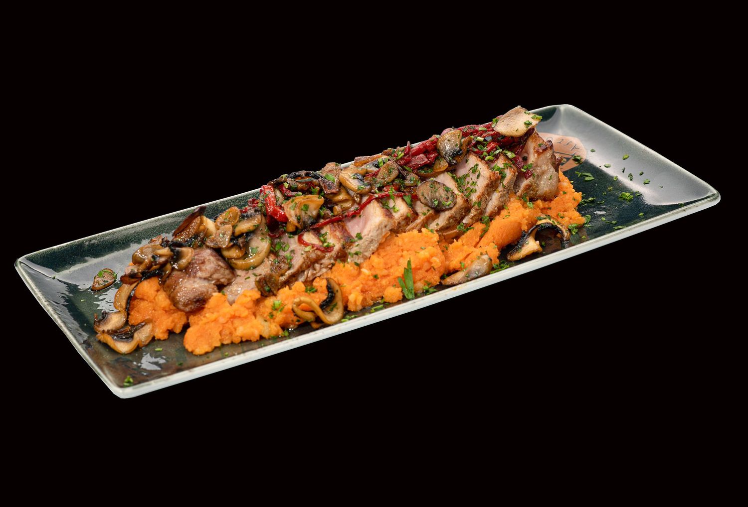 Champiñones asados ​​y otros aderezos servidos sobre puré de camote en un plato largo rectangular de vidrio. Tierra Astur