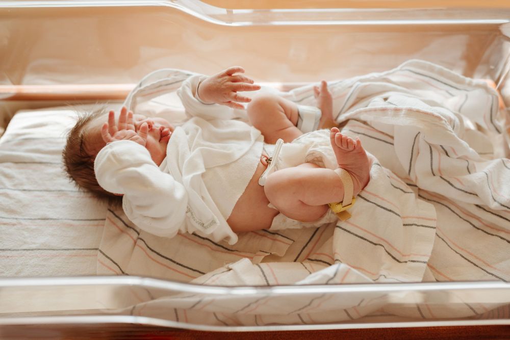 Newborn baby lying peacefully in white clothing on striped bedding.