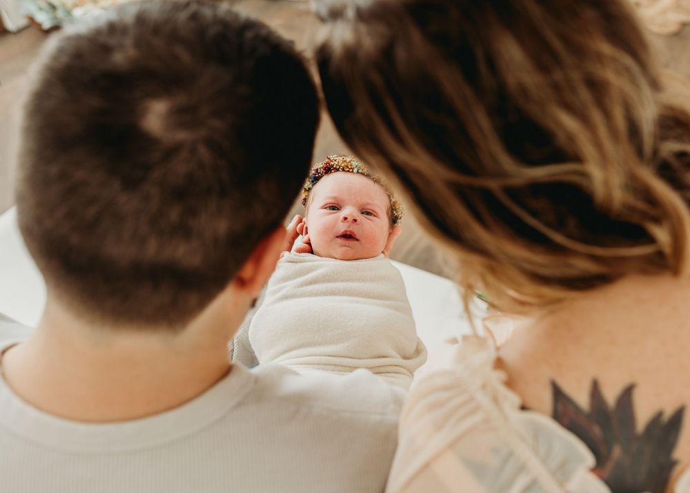 Newborn baby wrapped in white swaddle being admired by parents.