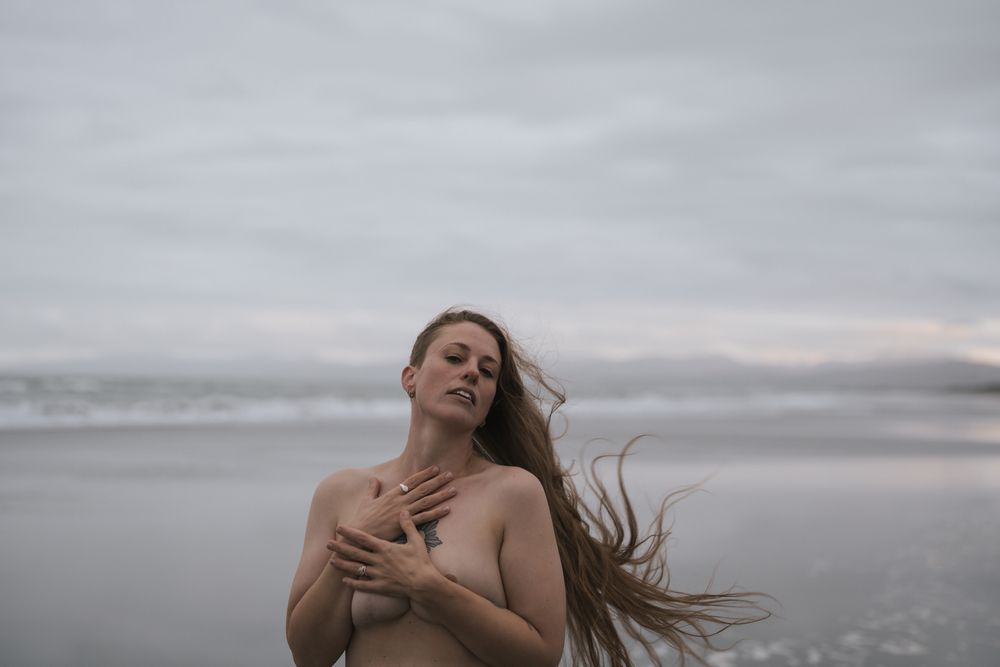 Woman with flowing hair poses at sunset on misty beach.