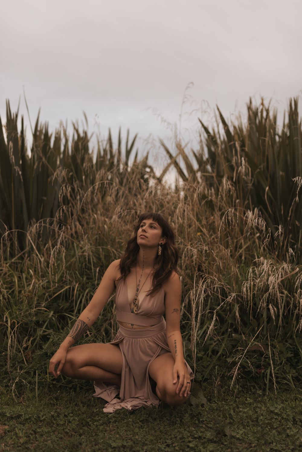 Figure in a flowing mauve dress sits in tall grass and pampas reeds during golden hour lighting.