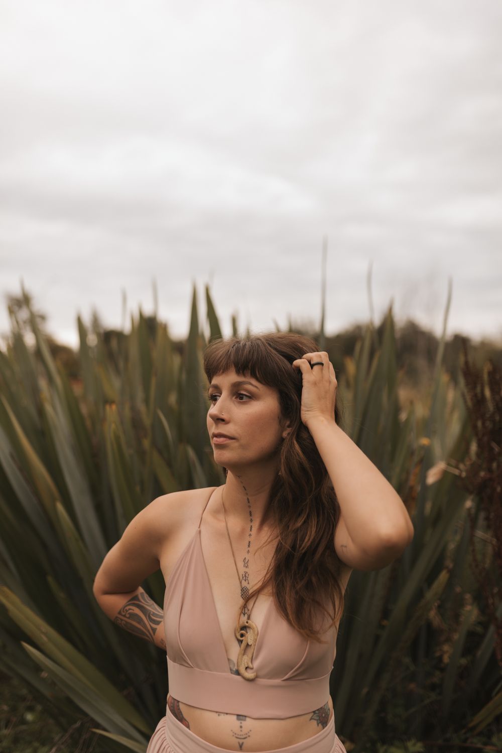 A woman in a beige crop top poses thoughtfully in front of desert plants on an overcast day.