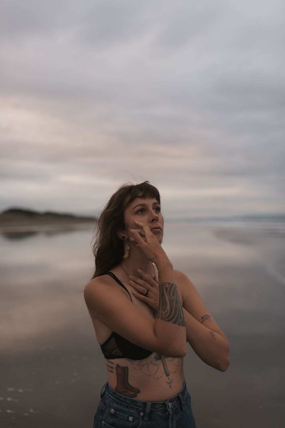 Artistic beach portrait at sunset with moody clouds and ocean backdrop showing person in denim and black top.