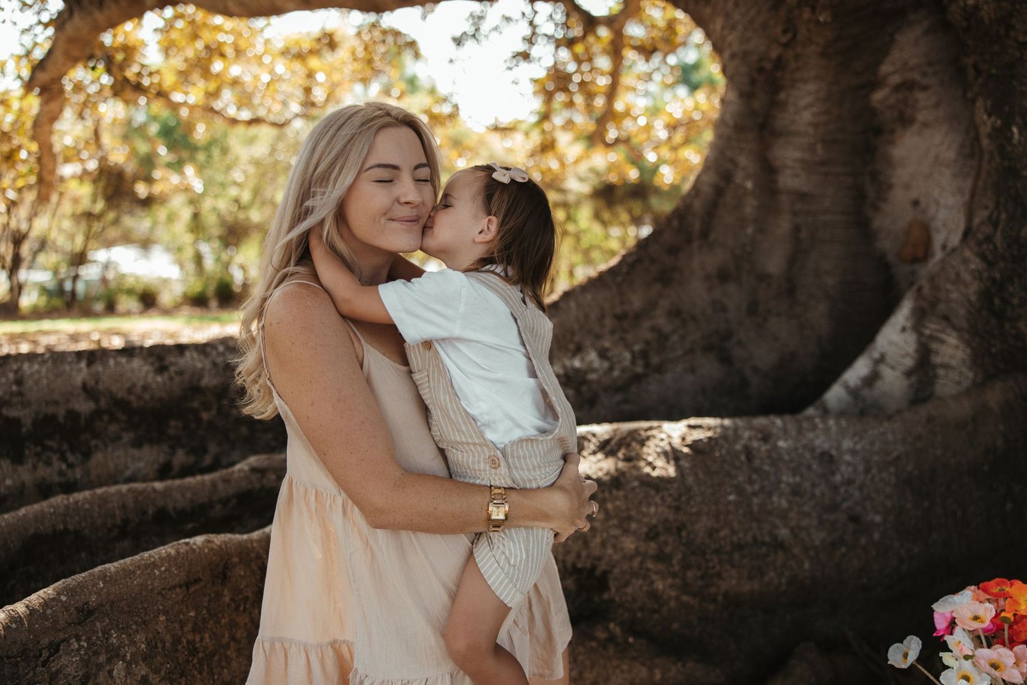 A tender moment is shared between parent and child under a large tree at sunset with warm golden light.