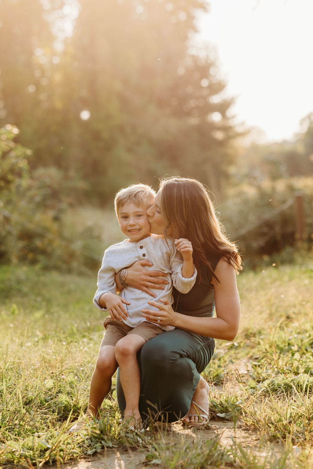 Intimate mother-child moment captured in golden sunlight outdoors.