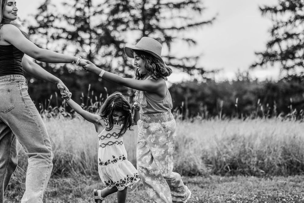 Playful black and white photo shows friends dancing and twirling in an open field.