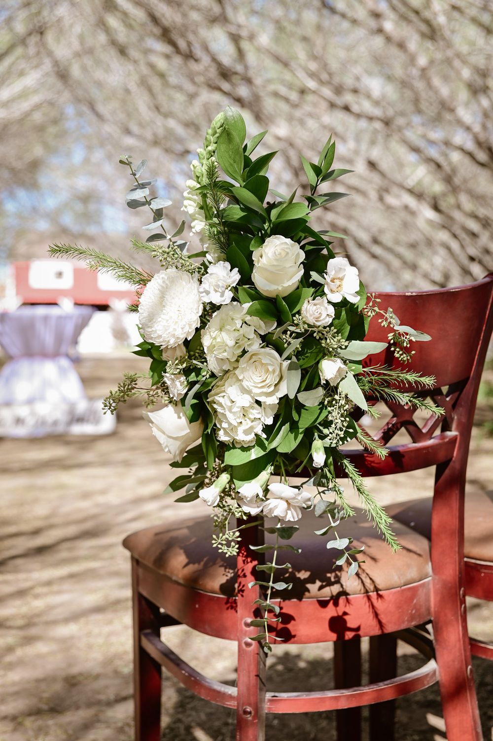 Elegant white floral arrangement with roses and greenery placed on a red vintage chair.