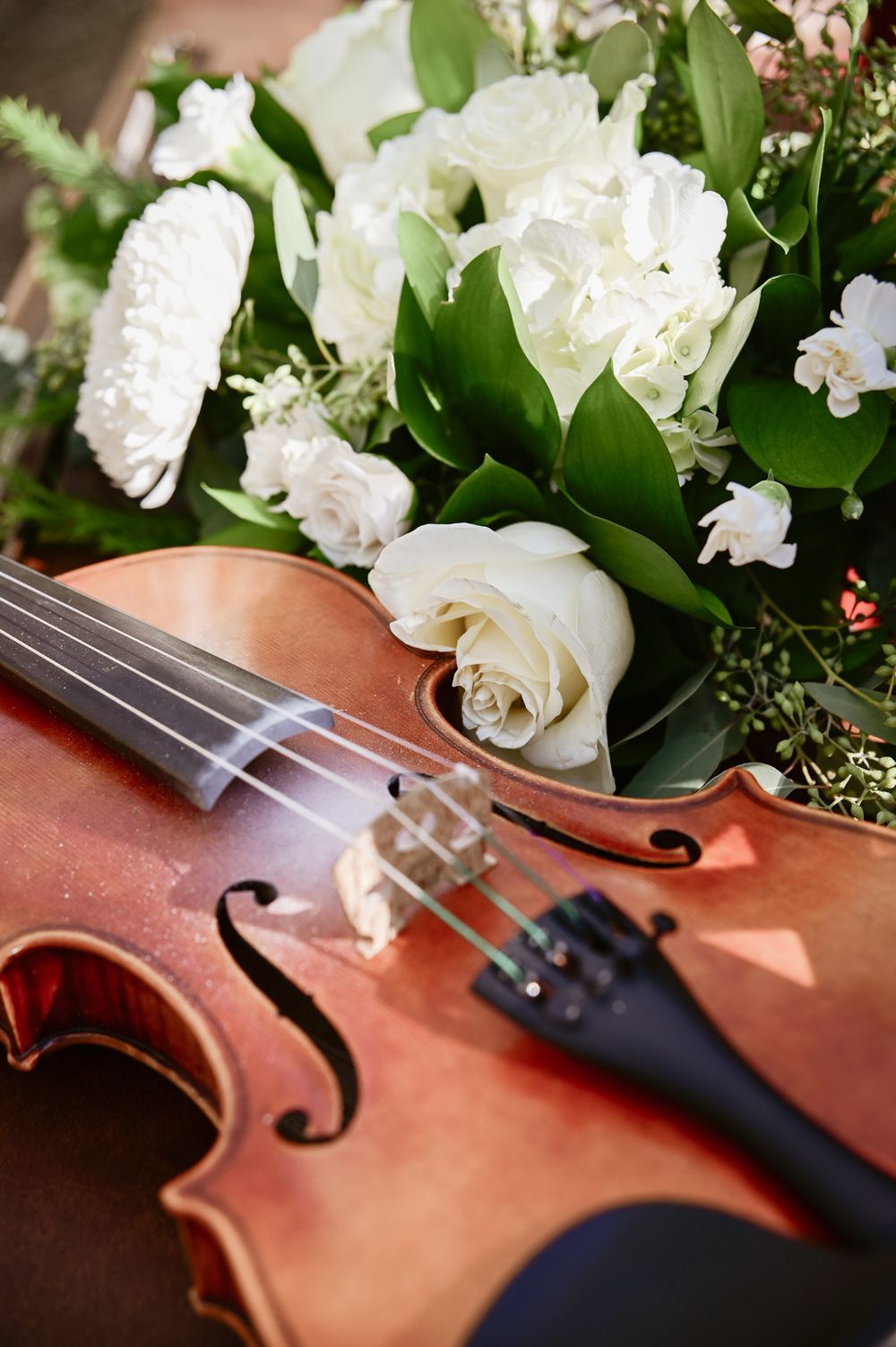 Violin displayed with white roses and greenery in an artistic wedding detail shot.