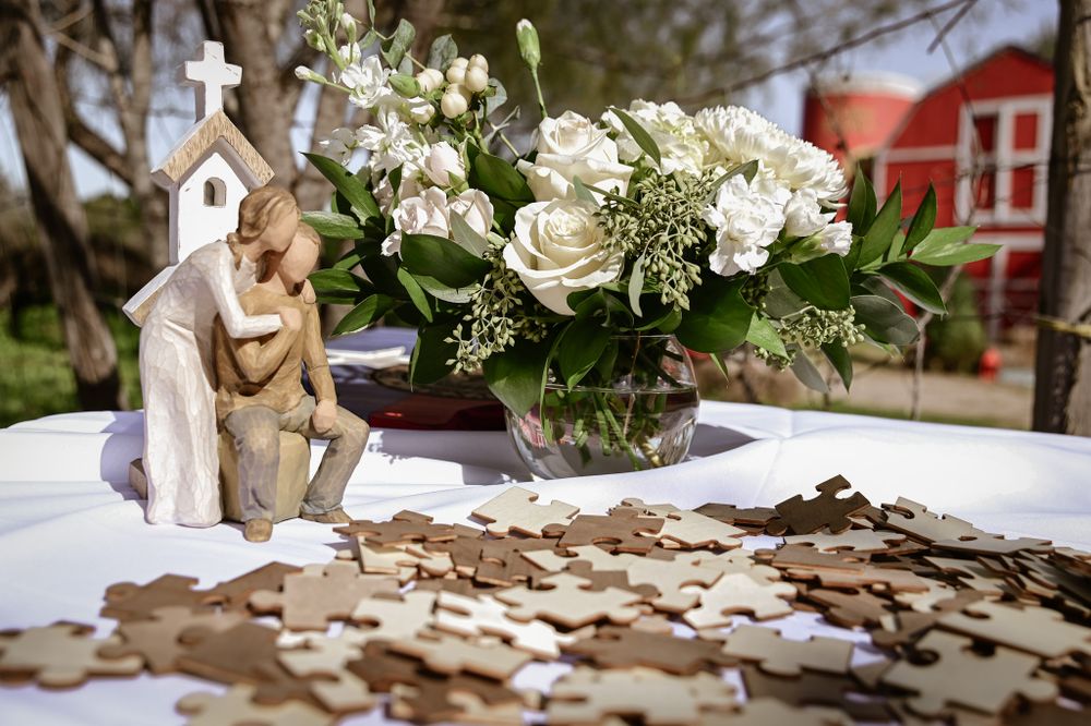 Wedding decor featuring religious figurine, coins, and white floral centerpiece on table.