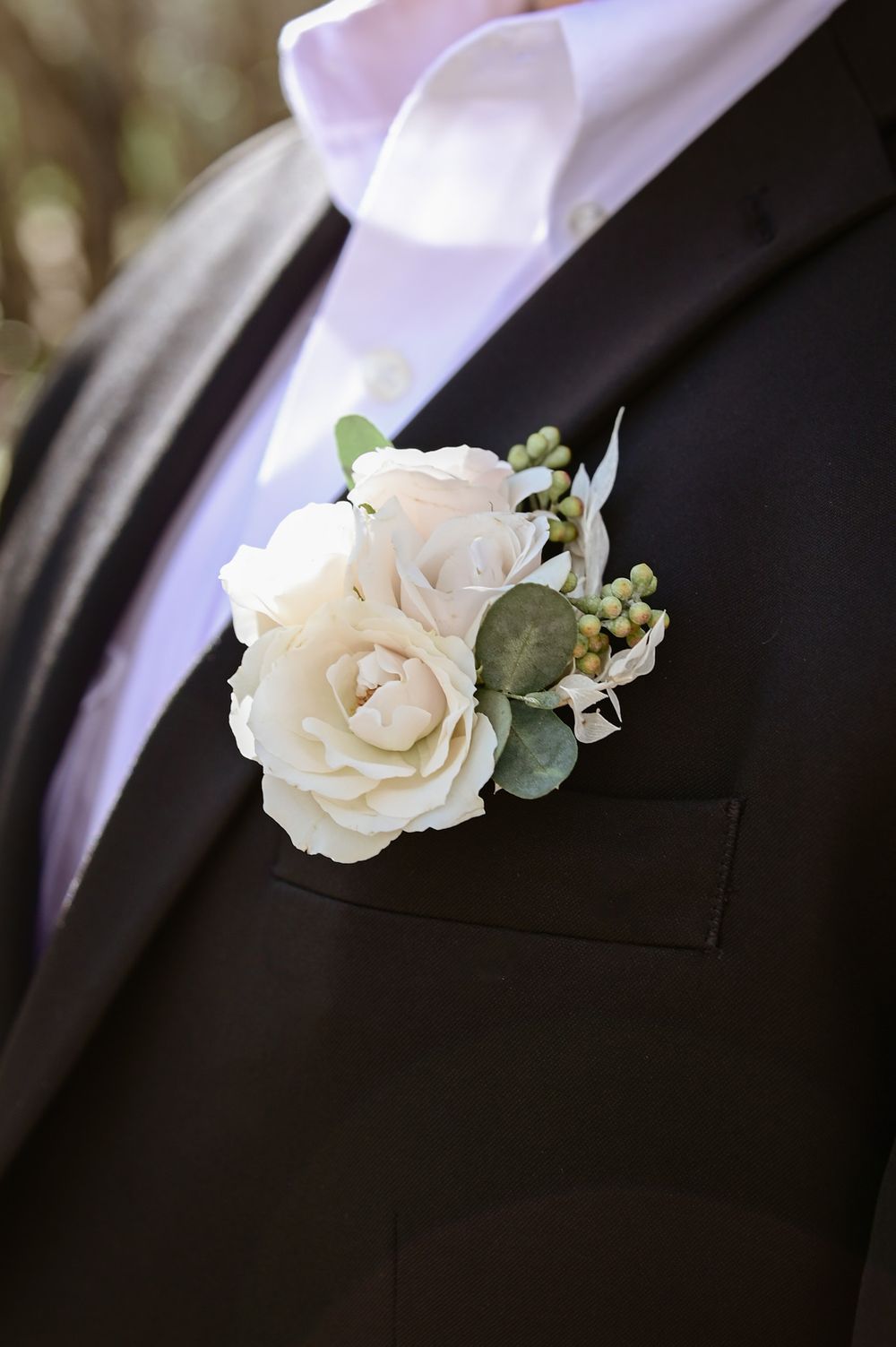 White rose boutonniere with eucalyptus on black suit lapel.