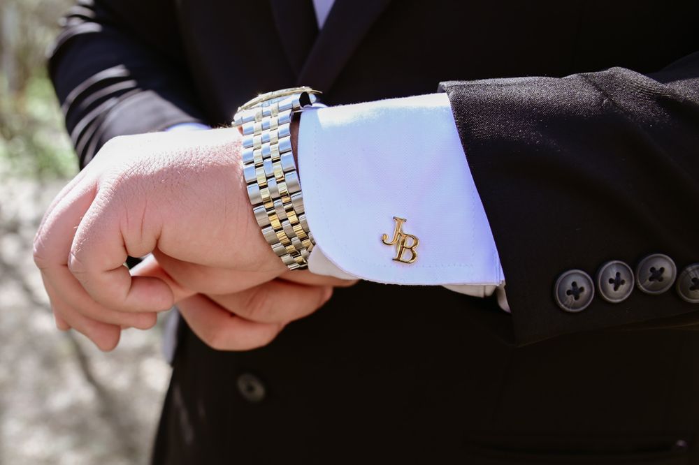 Close-up of a formal dress shirt cuff with monogrammed cufflink and two-tone metal watch.