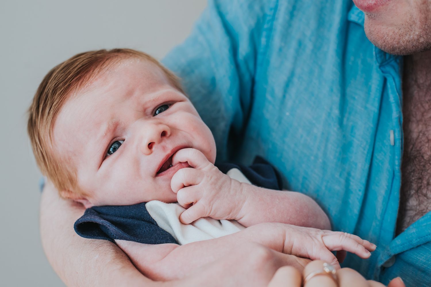 Newborn baby making a silly face in his dad's arms.