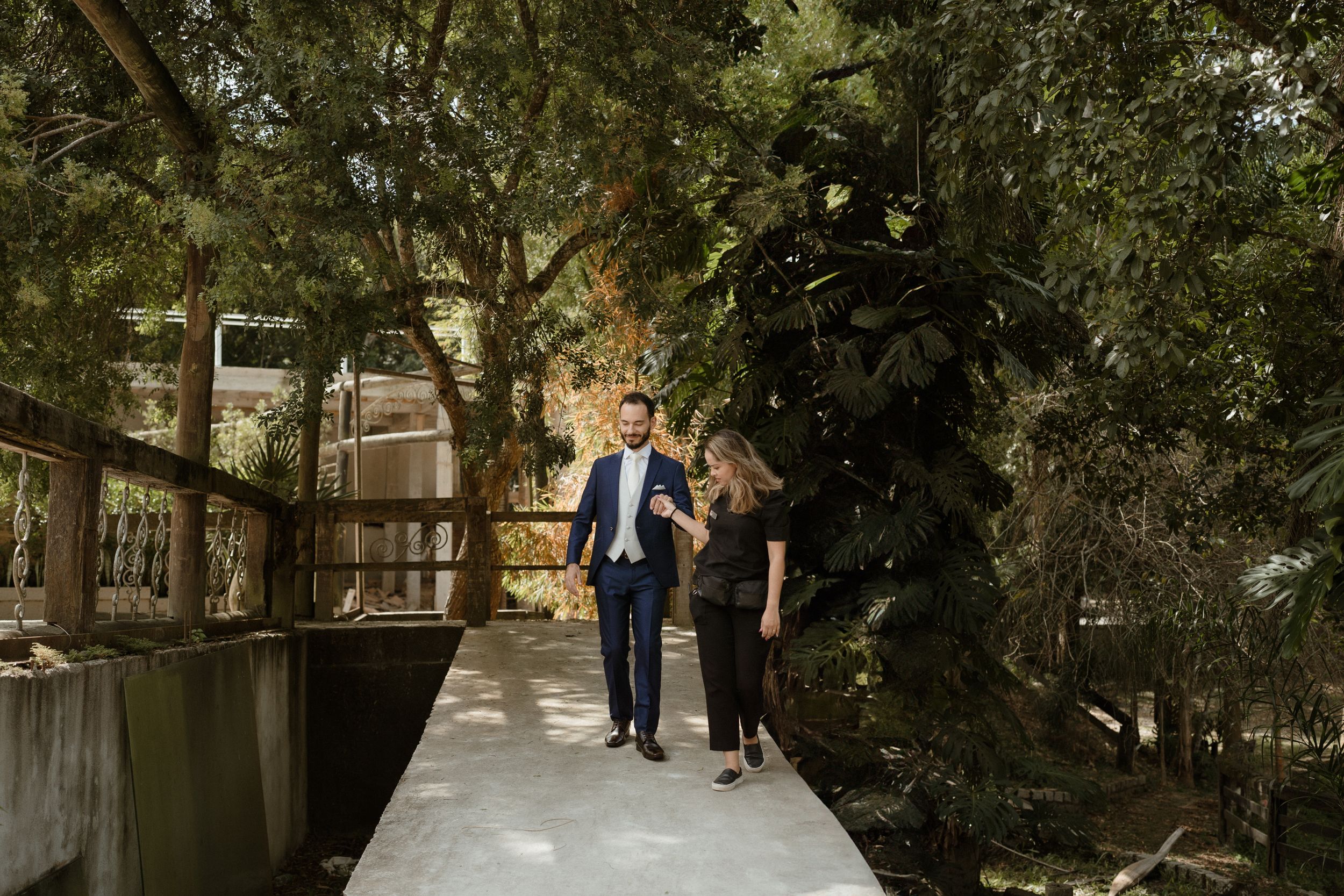 A couple strolls along a wooden walkway surrounded by lush forest greenery.