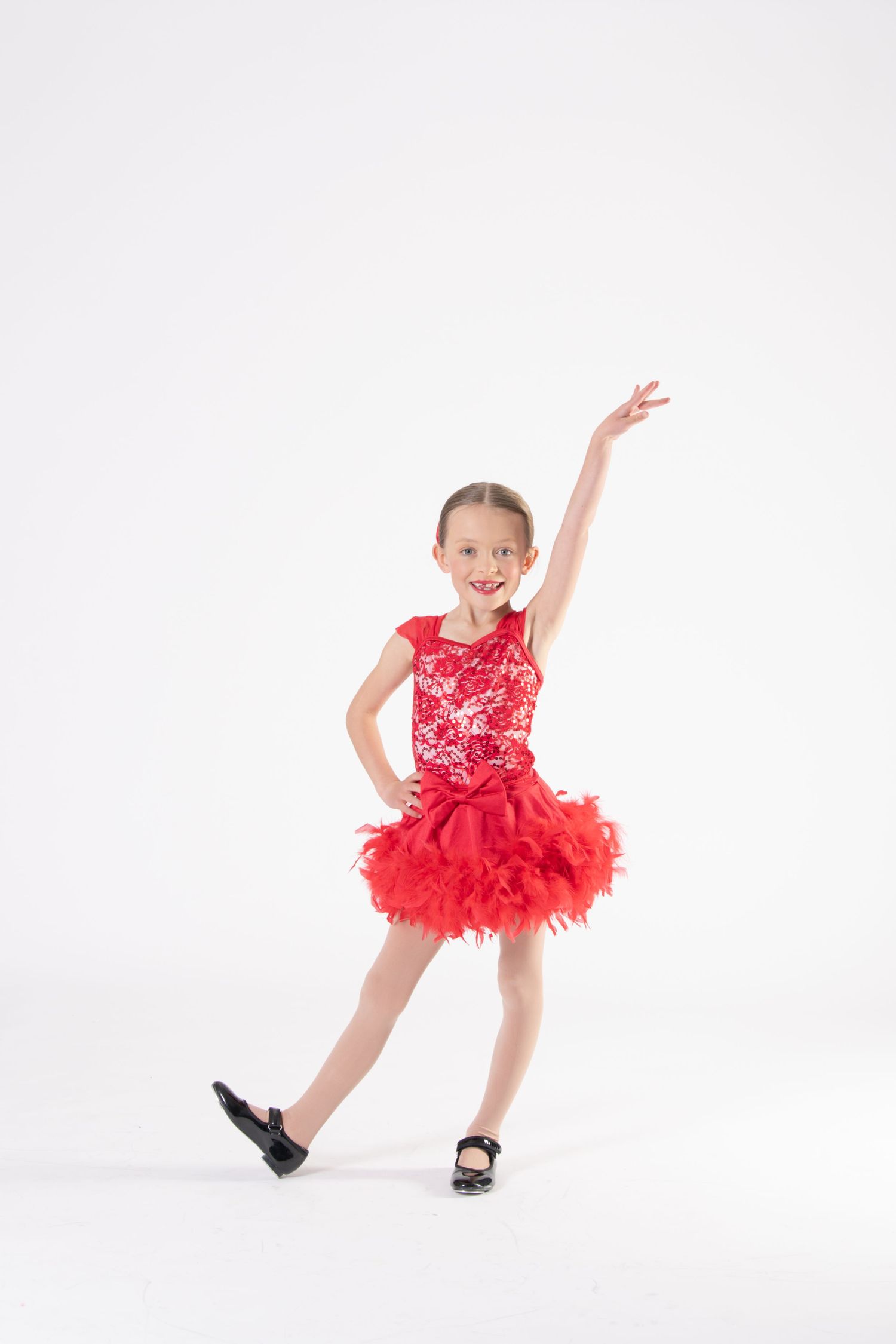 A dancer in a sparkly red costume with tutu strikes a tap dance pose against white background.