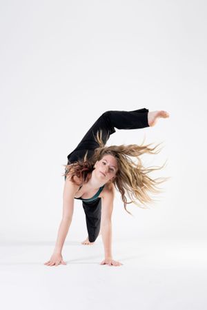 A dancer in black athletic wear performs a dynamic contemporary pose with flowing hair against a white background.