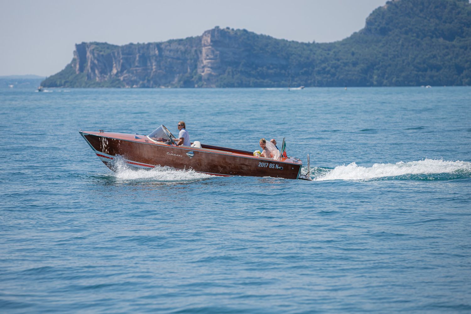 Wooden boat cruising across blue waters with cliffside mountains in background.