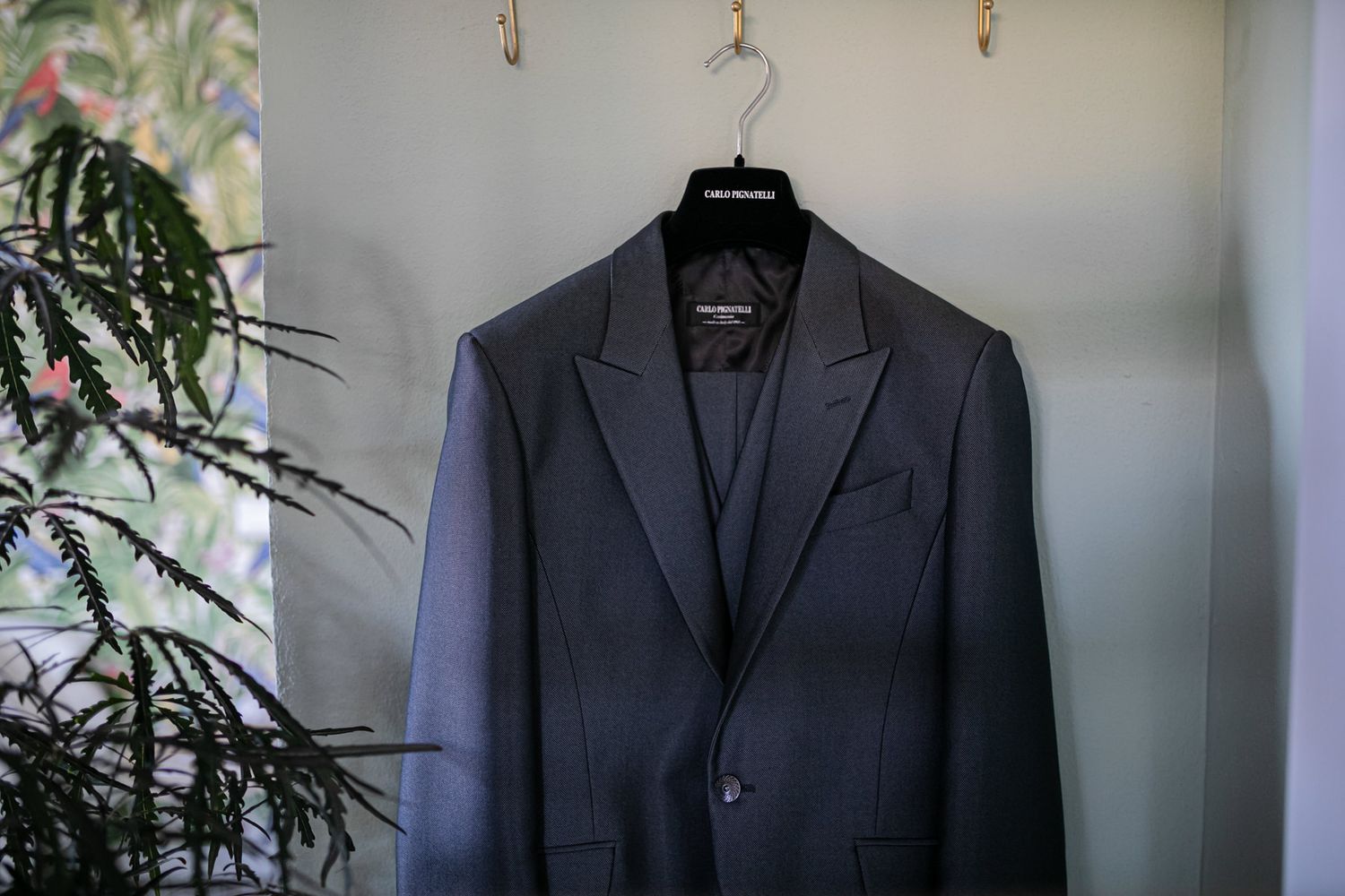 Dark suit jackets hanging neatly on wooden hangers against light wall.