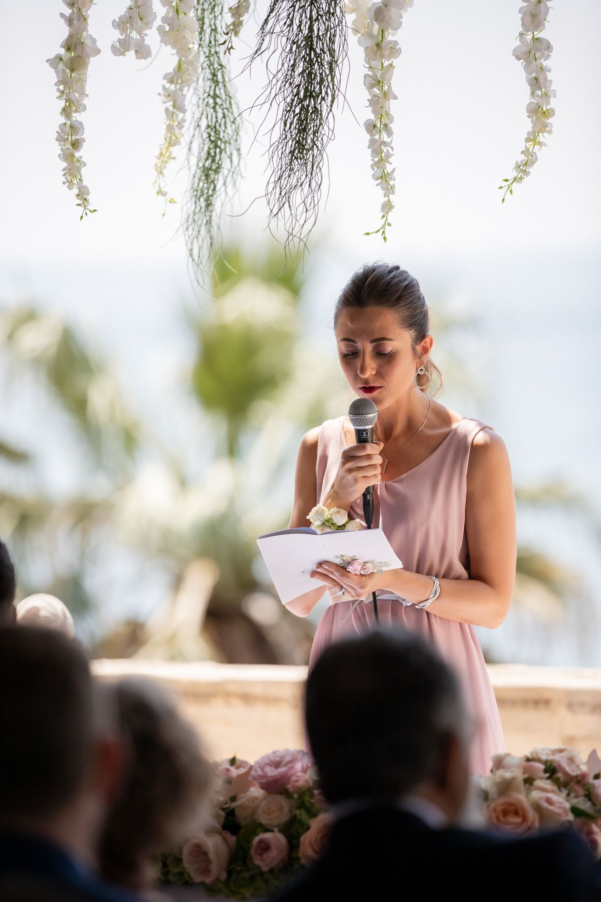 A wedding speech being delivered under hanging floral decorations at an outdoor venue.